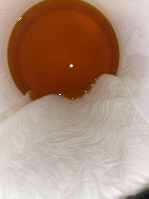 White bandana being dipped into a marigold dye bath, in a bucket, that is orange-brown in color.